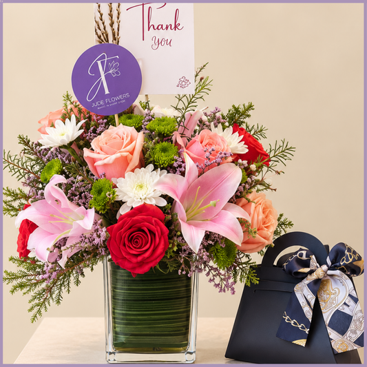 Grateful Indulgence gift with pink lily, orange roses, mixed flowers and chocolates in a black gift bag